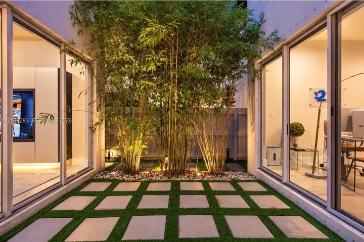Central atrium featuring large-format concrete pavers, integrated synthetic turf grid, mature bamboo specimens, and expansive floor-to-ceiling sliding glass doors