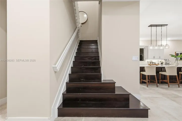 Staircase featuring dark wood-finish treads, white handrail, and white balusters, situated on stone-finish flooring with a multi-pendant light fixture and built-in cabinetry in the background