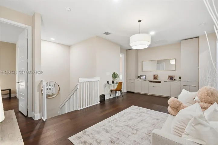 Dark wood-finish flooring, built-in floor-to-ceiling cabinetry with integrated storage, white spindle staircase railing, and a tiered drum pendant light fixture