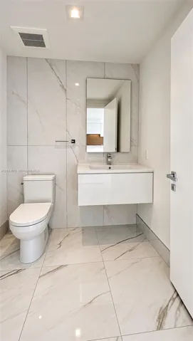 Floating vanity with a white integrated basin, floor-to-ceiling large-format tile wall, white stone-patterned floor tiling, rectangular mirror, and chrome single-handle faucet