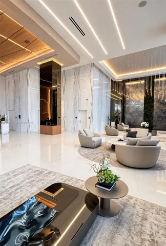 High-ceilinged lobby featuring large-format polished tile flooring, full-height stone wall cladding, integrated linear recessed lighting, and a tiered wood-panel ceiling feature