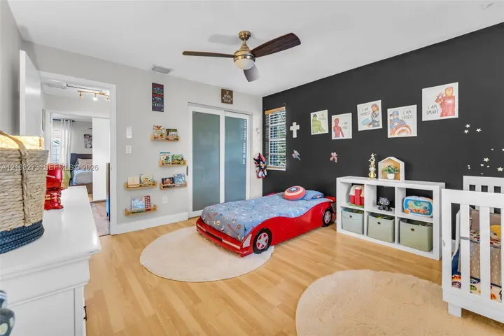 Wood-finish flooring, brushed metal ceiling fan with integrated light fixture, contrast accent wall, and sliding glass closet doors