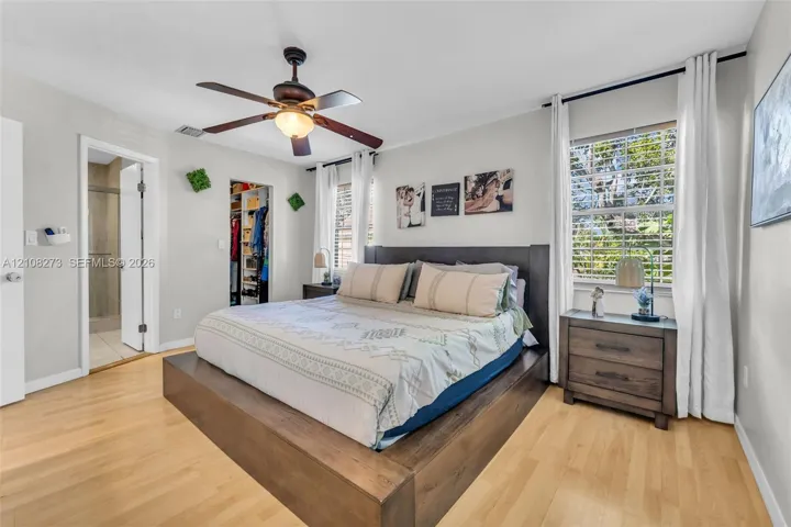 Bedroom featuring light wood-finish flooring, a ceiling fan with integrated lighting, and a walk-in closet with built-in organization