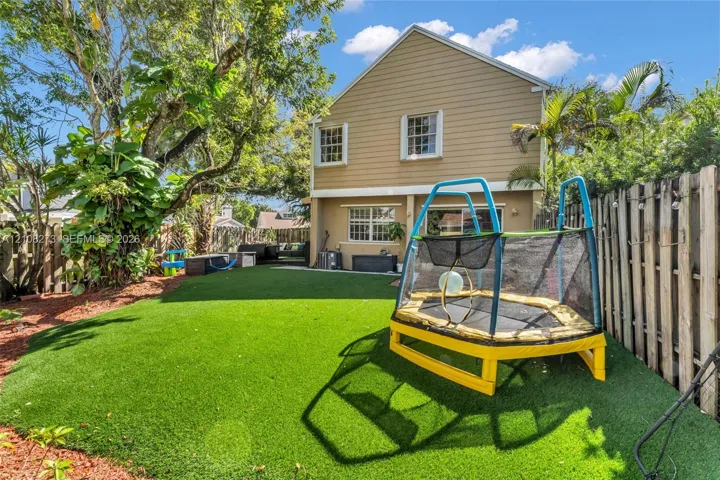Fenced backyard featuring synthetic turf, wood-siding exterior, and mature landscaping