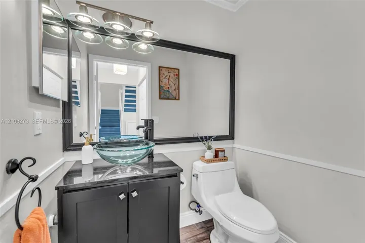 Black vanity with a stone countertop, circular glass vessel sink, matte black faucet, wall-mounted mirror, and multi-light vanity fixture