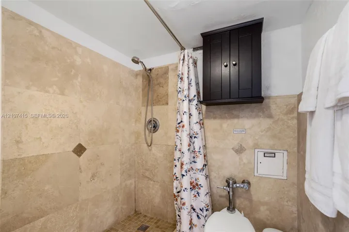 Shower enclosure featuring floor-to-ceiling stone-tile surround, mosaic tile flooring, built-in dark wood-finish cabinetry, and stainless steel hardware