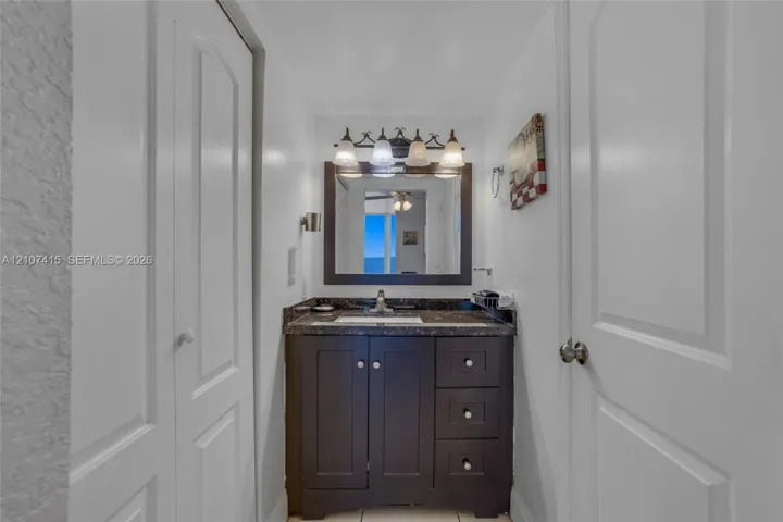 Dark cabinetry vanity featuring a stone countertop, an integrated rectangular sink, a framed mirror, and a multi-light fixture
