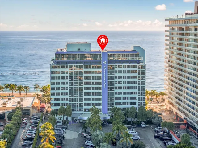 High-rise coastal building featuring floor-to-ceiling windows, an expansive glass-enclosed top level, and mature palm tree landscaping