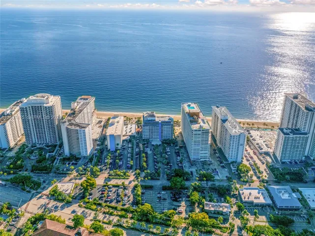 Aerial perspective of coastal high-rise properties featuring oceanfront positioning, proximity to sandy beach, and landscaped grounds with paved parking areas