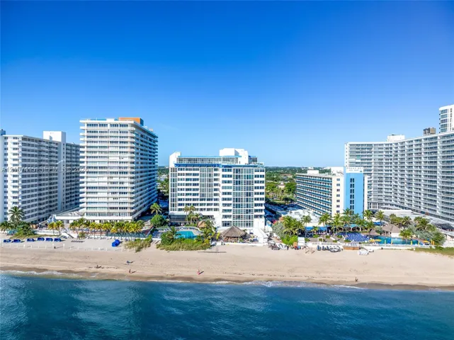 High-rise coastal architecture situated directly along a sandy shoreline with outdoor swimming pools and tropical palm tree landscaping