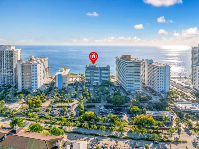 Aerial perspective of a high-rise residential structure positioned along the coastline featuring proximity to the ocean and mature palm tree landscaping