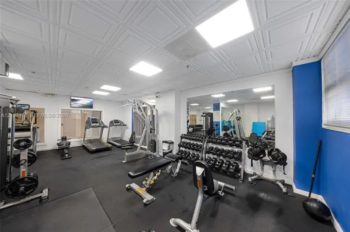 Fitness area featuring a coffered ceiling, recessed lighting, rubberized flooring, and wall-to-wall mirrors