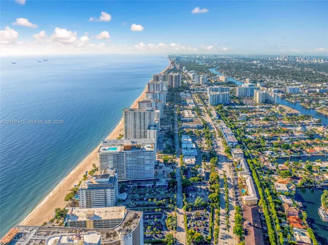 Aerial coastal perspective featuring a sandy beach, expansive ocean shoreline, high-rise residential architecture, and inland canal systems