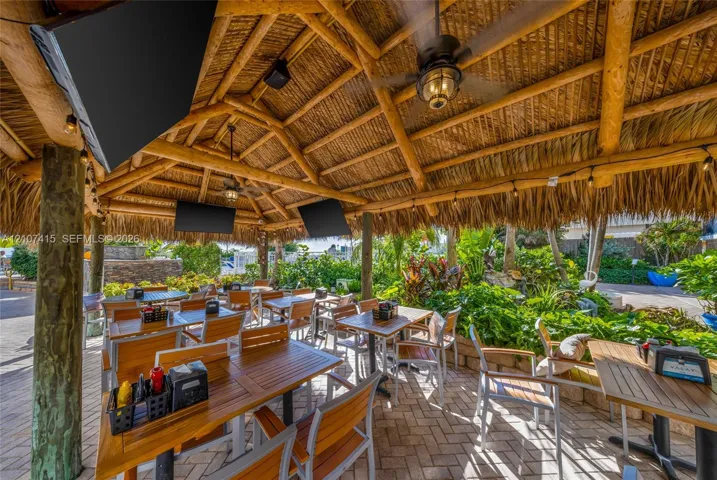 Covered outdoor pavilion featuring a thatched roof, exposed timber support beams, ceiling-mounted fans, and paver flooring