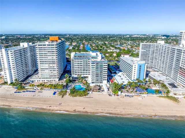 High-rise coastal property featuring direct ocean access, expansive sandy beachfront, multiple outdoor swimming pools, and landscaped grounds with mature palm trees