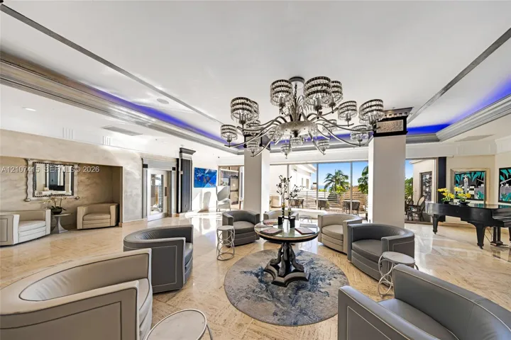 Expansive living area featuring polished stone flooring, recessed ceiling lighting with perimeter accent illumination, a tiered crystal chandelier, and floor-to-ceiling glass sliding doors