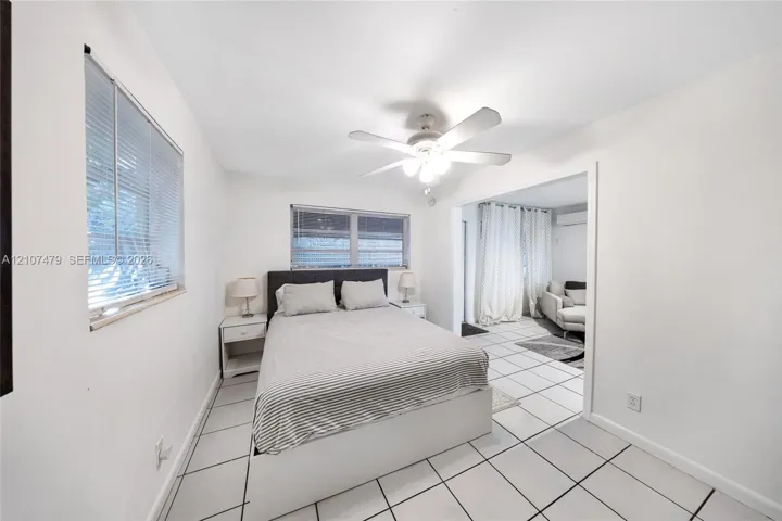 Interior space featuring large-format ceramic floor tiling, white walls, two windows with integrated blinds, and a central ceiling fan with integrated light fixture