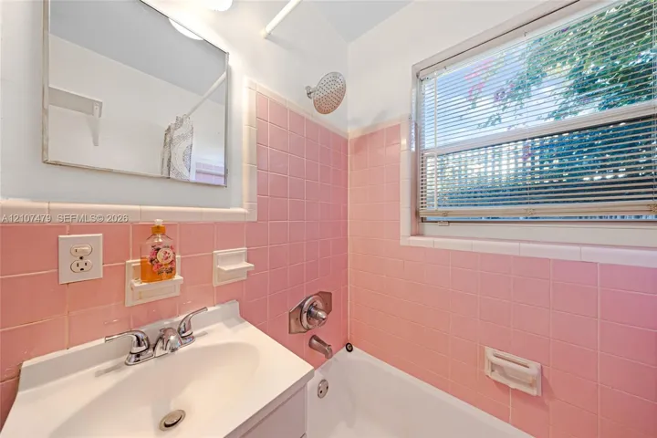 Bathroom featuring pink ceramic wall tiling, a white porcelain sink with a polished chrome widespread faucet, a wall-mounted medicine cabinet, and a shower-tub combination with a chrome showerhead