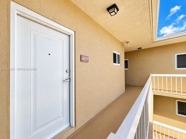 Entryway featuring a white paneled door with a metallic deadbolt, exterior wall-mounted lighting, and a white metal safety railing