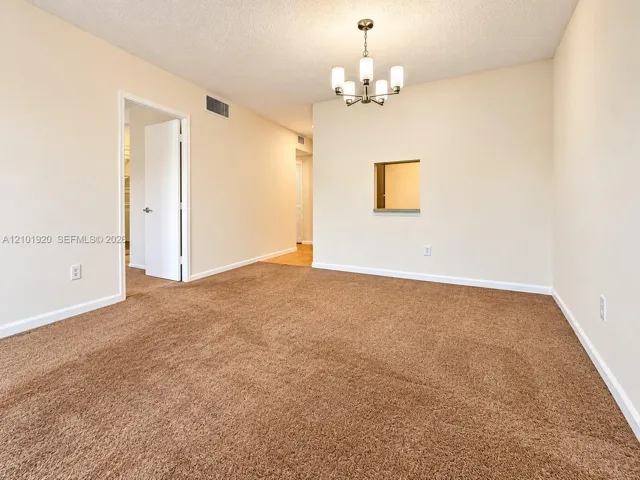 Interior space featuring neutral wall tones, wall-to-wall carpeting, a five-light chandelier, and a decorative interior pass-through window