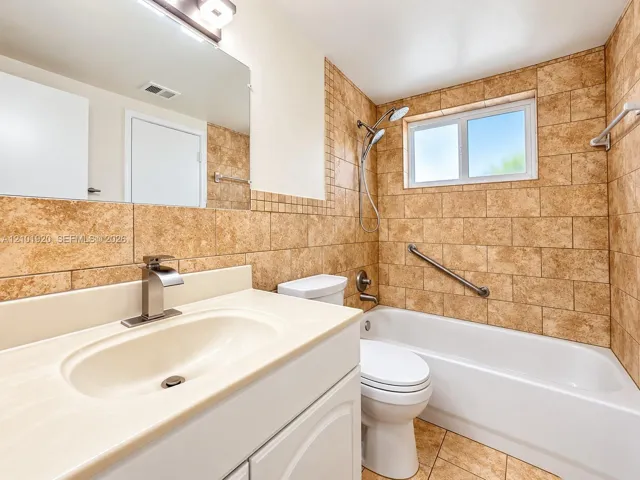 Bathroom featuring a white vanity with a solid surface countertop, an undermount sink, a tub-shower combination with floor-to-ceiling tile surround, and a wall-mounted grab bar