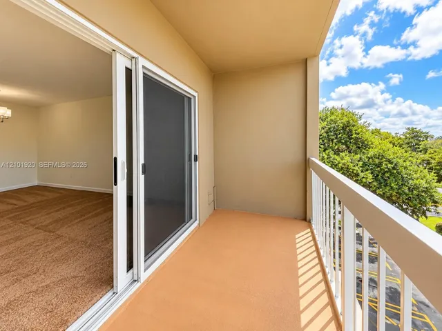 Covered private balcony with white metal railing, smooth-surface flooring, and sliding glass door entry
