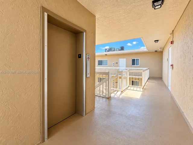 Elevator access with metal door frame, textured exterior walls, and white railing balcony system