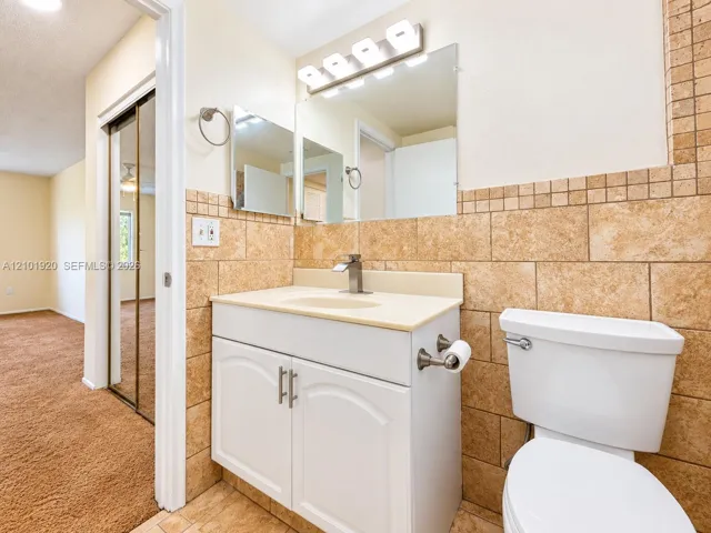 Bathroom featuring a vanity with white cabinetry and a solid-surface countertop, a rectangular four-light fixture, tiled wall accents, and a mirrored medicine cabinet