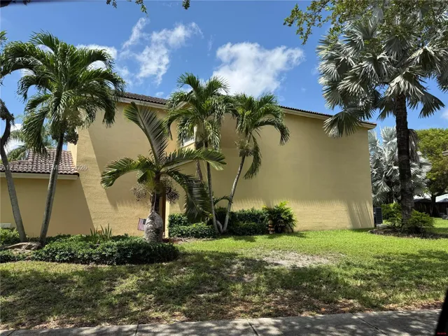 Two-story stucco exterior featuring a tile roof, manicured lawn, and mature palm trees
