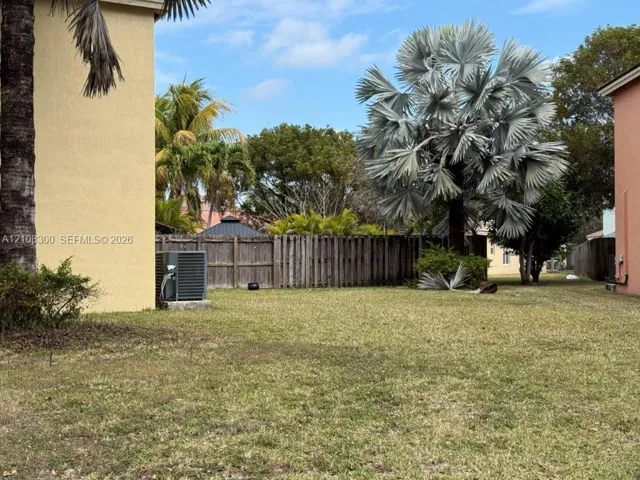Expansive side yard and rear yard featuring a manicured lawn, established palm trees, and a wooden privacy fence