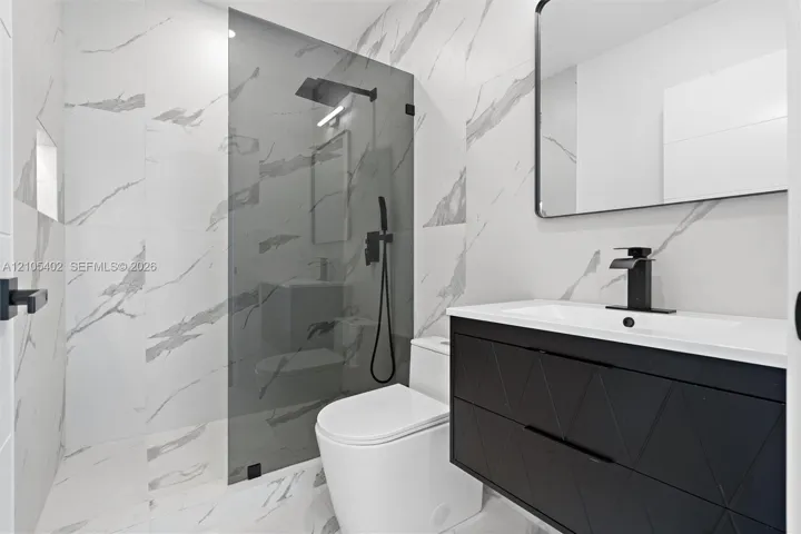 Modern bathroom featuring large-format wall and floor tile with a veined pattern, walk-in shower with glass panel, matte black plumbing fixtures, and a textured floating vanity with integrated sink