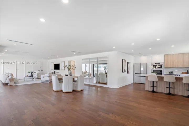 Open-concept interior featuring wood-finish flooring, recessed lighting, a built-in mirrored wall, and a kitchen equipped with wood-finish cabinetry and a tiered island