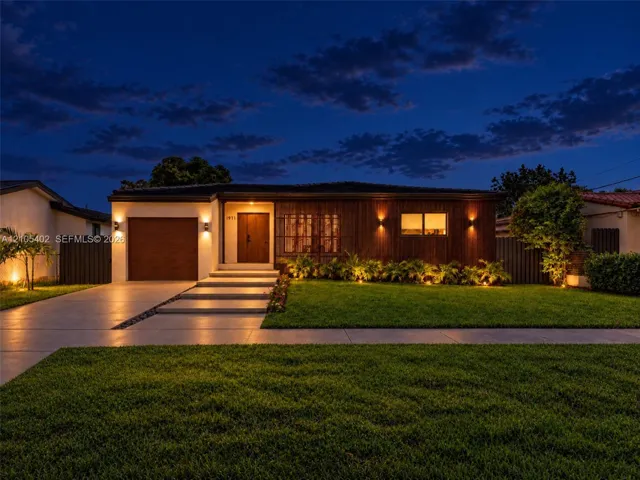 Modern single-story exterior featuring a wood-panel façade, integrated wall sconce lighting, solid wood front door, horizontal-slat garage door, and concrete entry steps