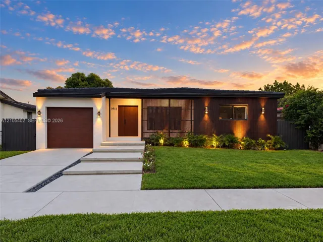 Single-story residence featuring a mid-century modern aesthetic, wood-paneled exterior accents, a concrete driveway with stone drainage detail, a stepped concrete entryway, and wall-mounted exterior lighting