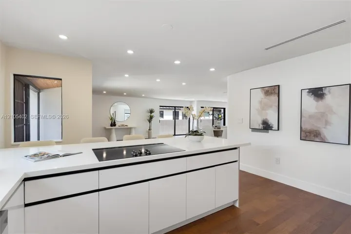 Kitchen island featuring white flat-panel cabinetry, a solid surface countertop, and an integrated cooktop, complemented by recessed lighting and wood-finish flooring