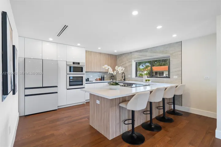 Kitchen featuring flat-panel cabinetry, a central island with a solid surface countertop, wood-finish flooring, integrated wall ovens, and a stone-style tile backsplash