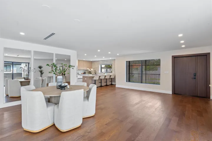 Open-concept interior featuring wood-finish flooring, recessed lighting, a built-in wall mirror, and a solid wood front door