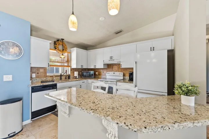 Kitchen featuring Granite countertops, white cabinetry with dark hardware, stone-tile backsplash, tile flooring, and pendant lighting