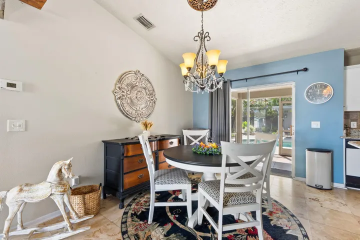 Vaulted ceiling with an ornate multi-arm chandelier, large-format tile flooring, and sliding glass door with external patio access