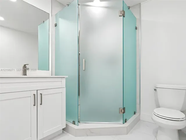 Bathroom featuring a white vanity cabinet, a wall-mounted mirror, a corner shower enclosure with frosted glass panels, and tile flooring