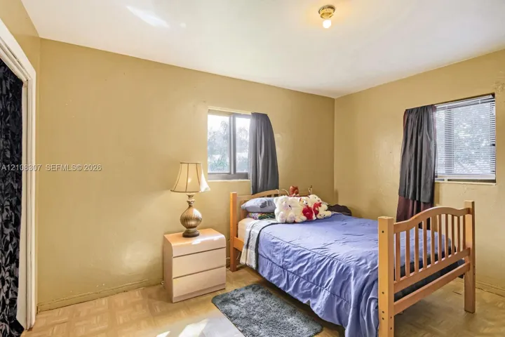 Bedroom featuring light-toned flooring, two windows providing natural light, and a ceiling-mounted light fixture