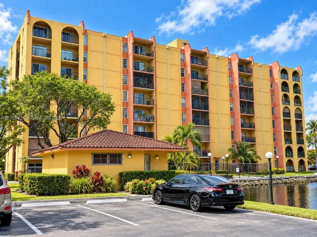 Multi-story residential building featuring arched balcony detailing, stucco exterior finish, attached private balconies, and waterfront landscaping
