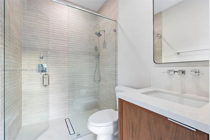 Walk-in shower featuring textured wall tile, glass enclosure, and rainfall showerhead, paired with a wood-finish vanity, solid-surface countertop, and wall-mounted faucet