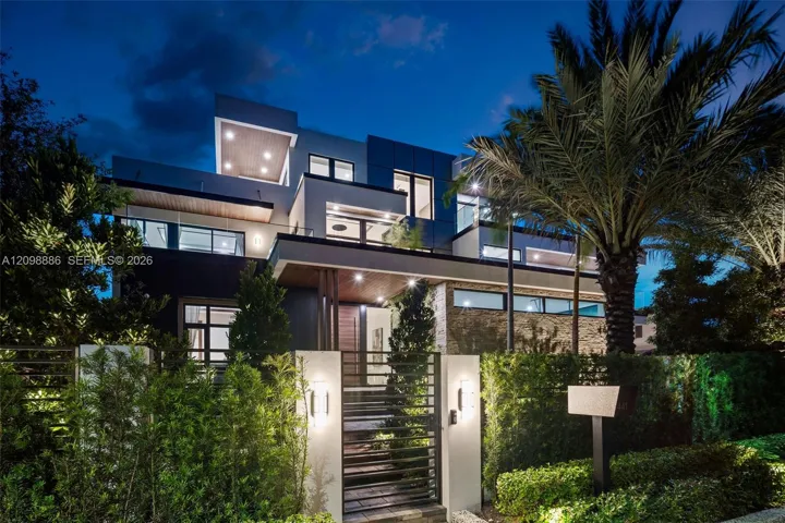 Modern multi-level exterior featuring clean geometric lines, stacked stone accents, recessed ceiling lighting, glass balcony railings, and a gated entrance