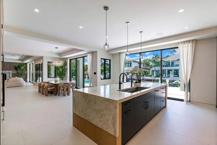 Kitchen featuring a large central island with waterfall-edge countertop, dark cabinetry, recessed lighting, and expansive sliding glass doors