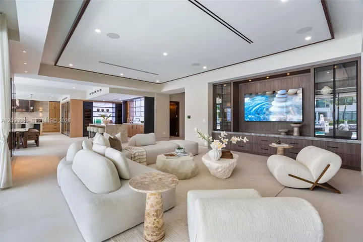 Open-concept living space featuring a recessed tray ceiling, custom built-in cabinetry with integrated display lighting, and large-format tile flooring