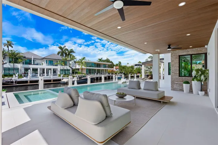 Covered patio featuring a wood-plank ceiling, recessed lighting, and dual ceiling fans, complete with a stone-accented wall and a custom pool bordering the canal