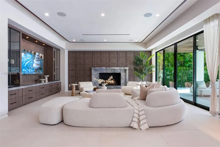 Living area featuring custom wood-finish built-in cabinetry, stone-surround fireplace, dark wood paneled accent wall, recessed ceiling lighting, and floor-to-ceiling sliding glass doors