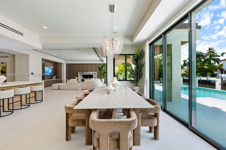 Open-concept interior featuring large-format tile flooring, a statement crystal chandelier, built-in cabinetry, a fireplace with stone surround, and floor-to-ceiling sliding glass doors opening to a pool and canal