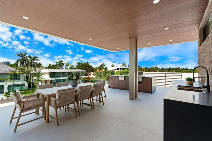 Covered terrace featuring wood-finish ceiling, recessed lighting, outdoor kitchen with integrated grill and cabinetry, and horizontal metal railing